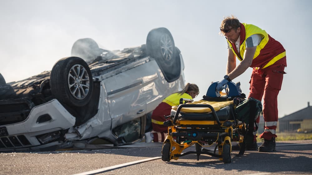 Paramedics and firefighters respond to a car crash, preparing the stretchers to rescue an injured victim trapped in a rollover vehicle