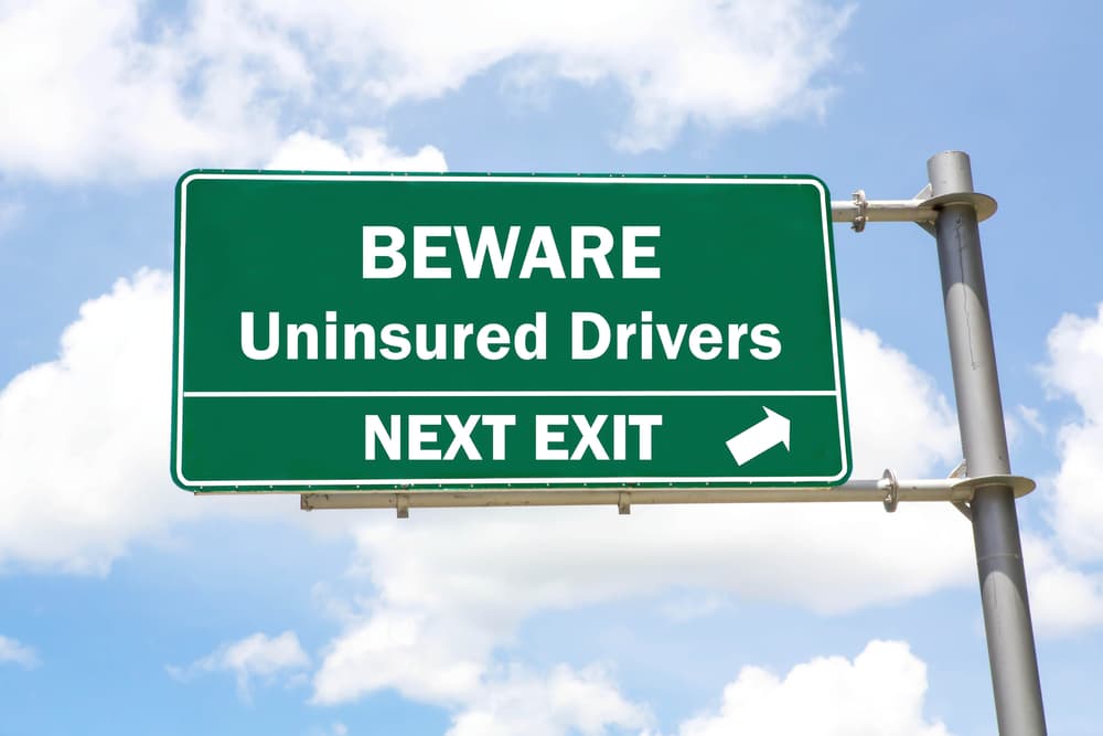 Green overhead road sign with a Beware of Uninsured Drivers Next Exit
