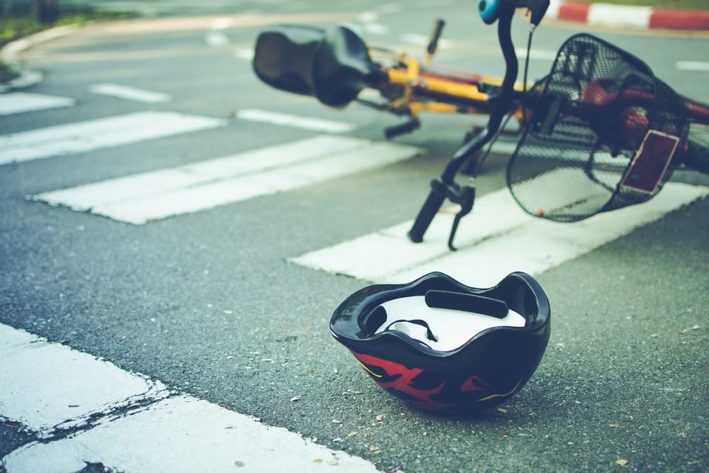 Bicycle and helmet on the ground at a crosswalk following a crash, representing the aftermath of a bicycle accident.