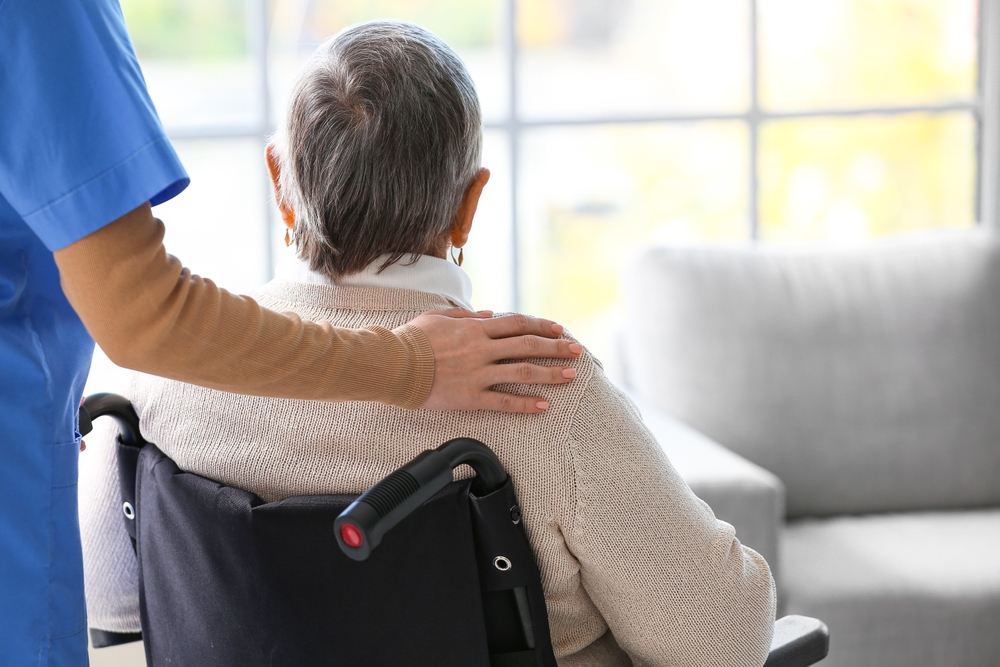 Caregiver placing a reassuring hand on an elderly person in a wheelchair, illustrating concerns about elder abuse and supportive interventions.